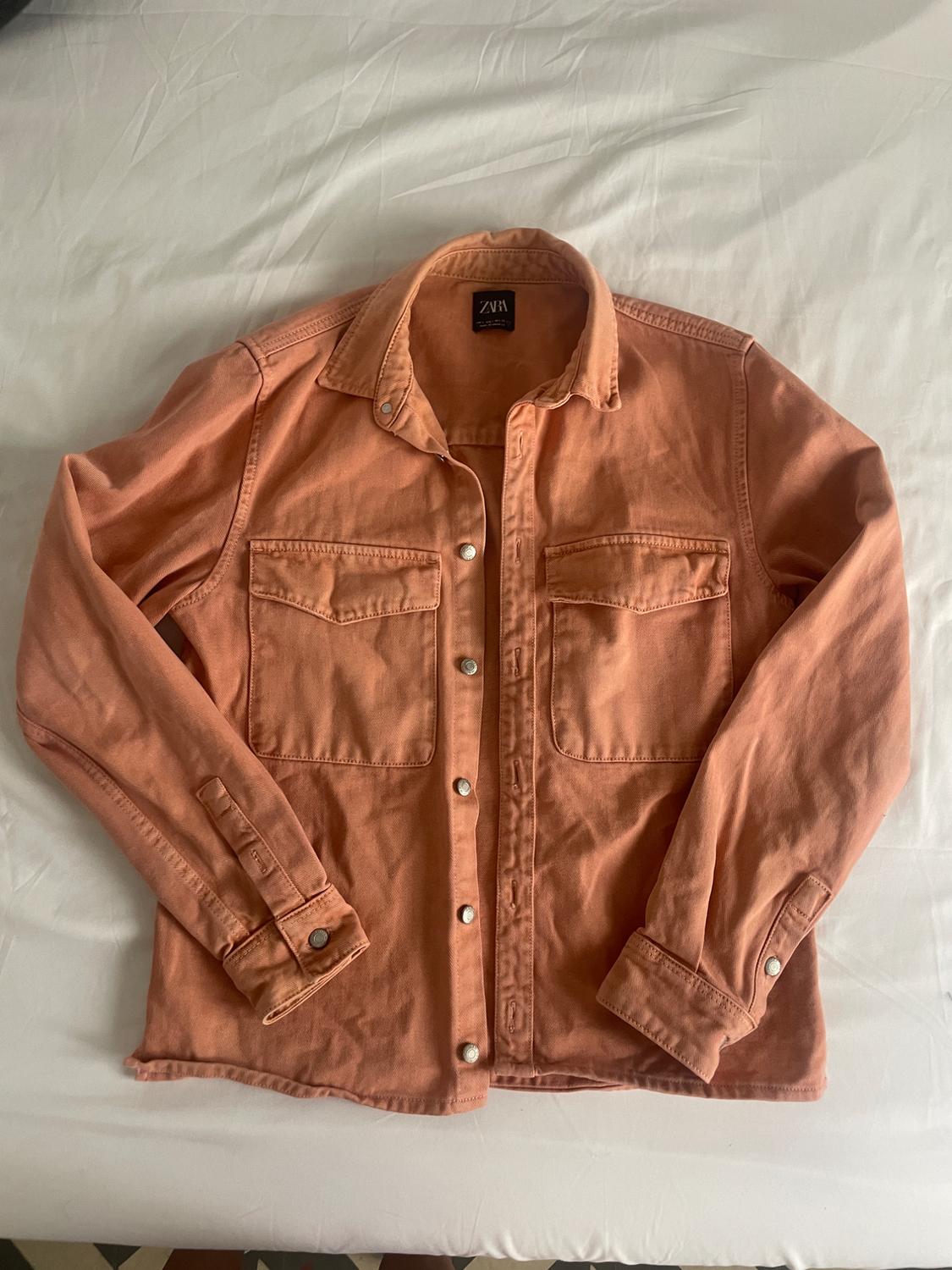 Salmon-pink button-down shirt with front pockets, laid out flat on a white sheet. ZARA label on the collar.