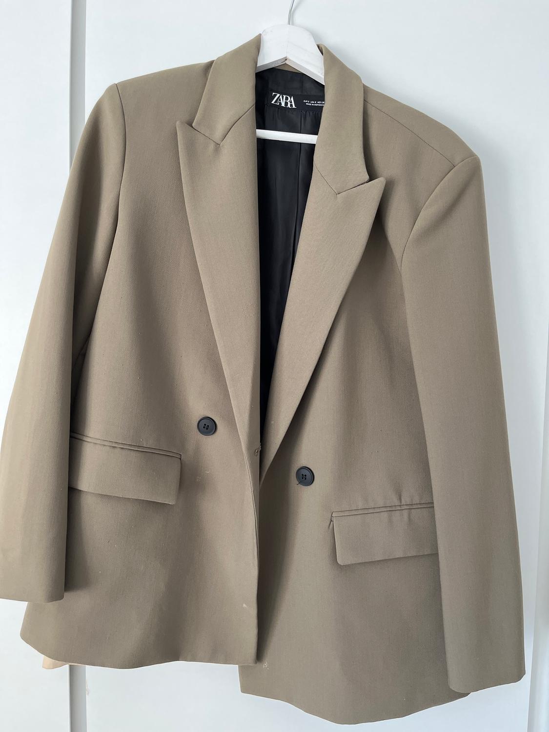 Beige double-breasted jacket hanging on a white hanger. Visible label with the text "ZARA" inside.