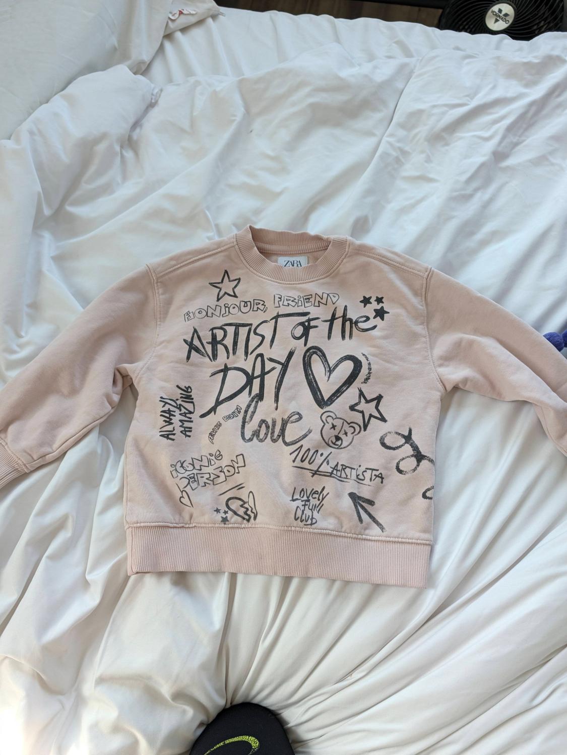 Pink sweatshirt in bed with drawings and text: BONJOUR FRIEND ARTIST of the DAY love ALWAYS AMAZING ICONIC PERSON 100% ARTISTA LOVELY FUN CLUB