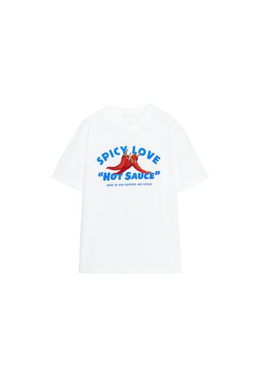Front view of a white t-shirt with the text "SPICY LOVE 'HOT SAUCE'" and a graphic of red chili peppers. Crew neck, short sleeves.