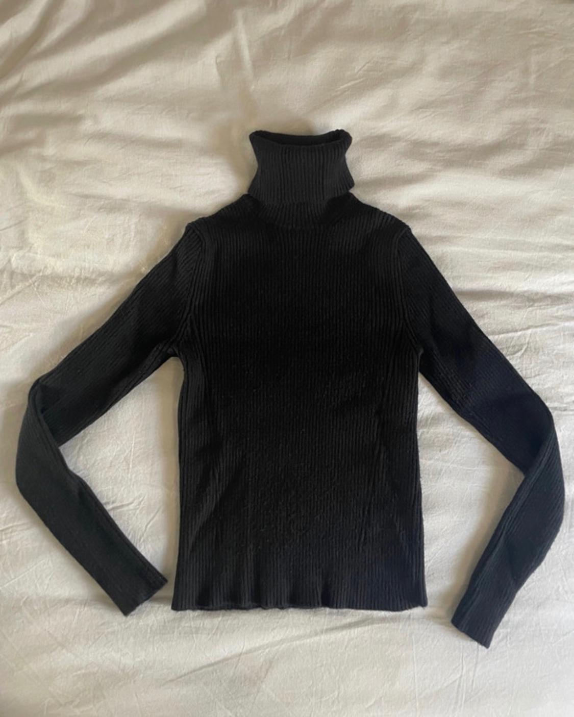 Black ribbed roll-neck jumper with long sleeves, laid out on a crumpled white sheet.