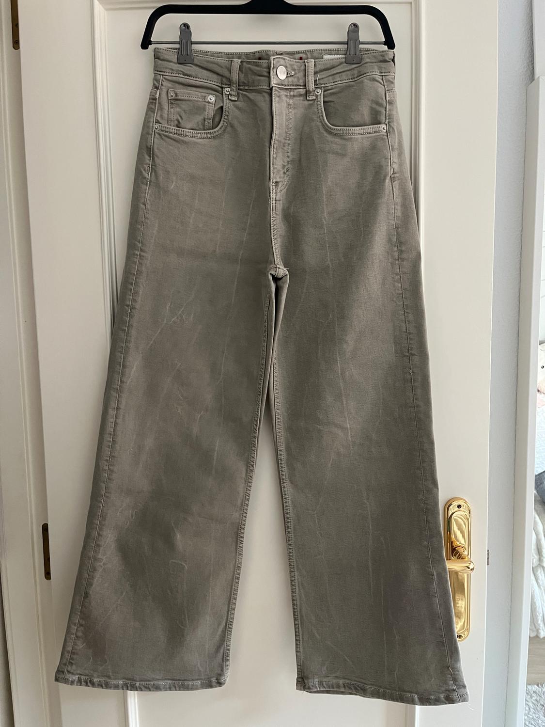 Grey wide-leg trousers hanging on a black hanger over a white door with a gold handle.