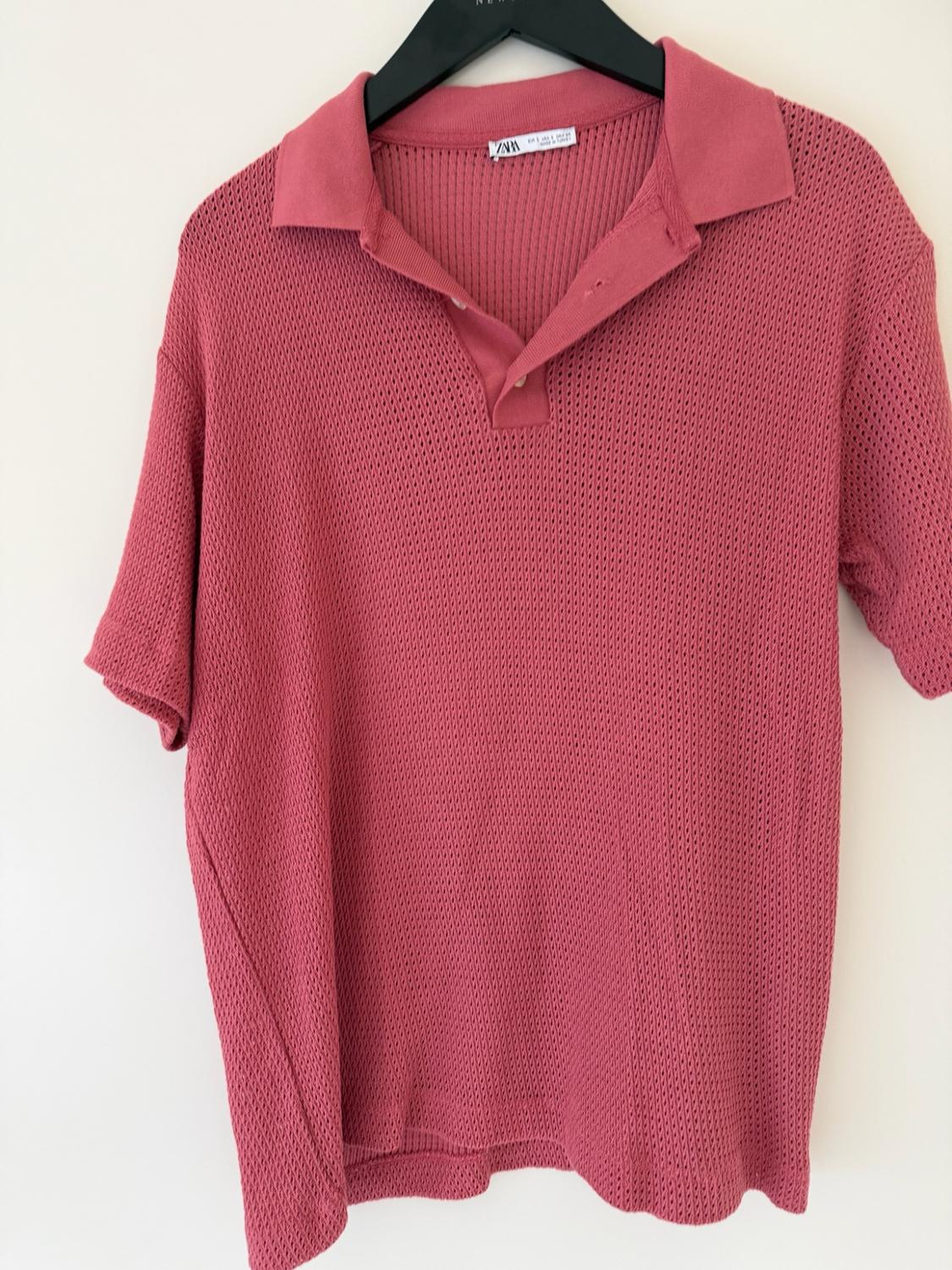 Pink short-sleeved polo shirt in openwork knit fabric, hanging on a black hanger against a white background. Label with the text ZARA.
