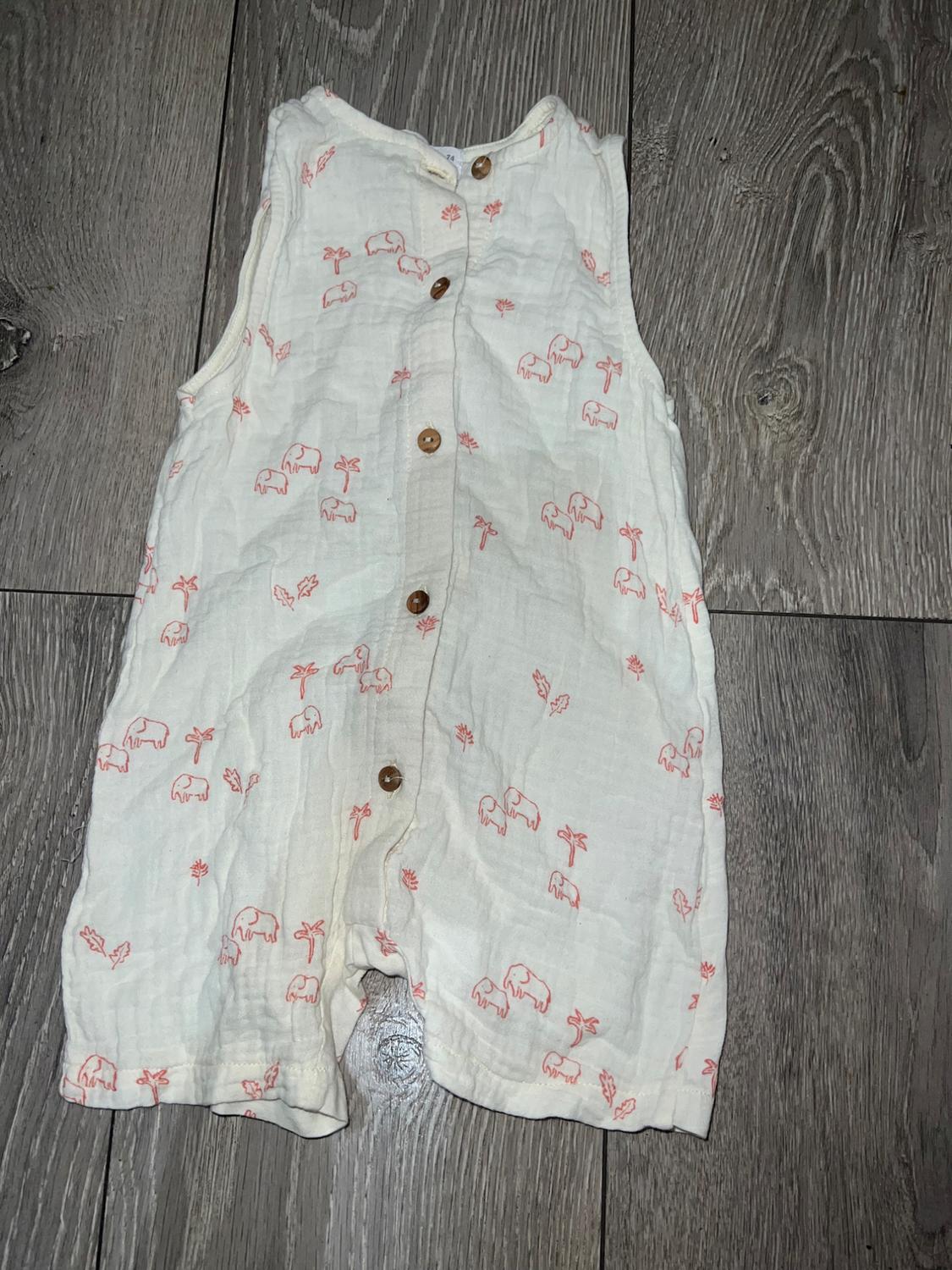 White baby romper with pink elephant and palm tree print, wooden buttons at the front, on a grey wooden floor.