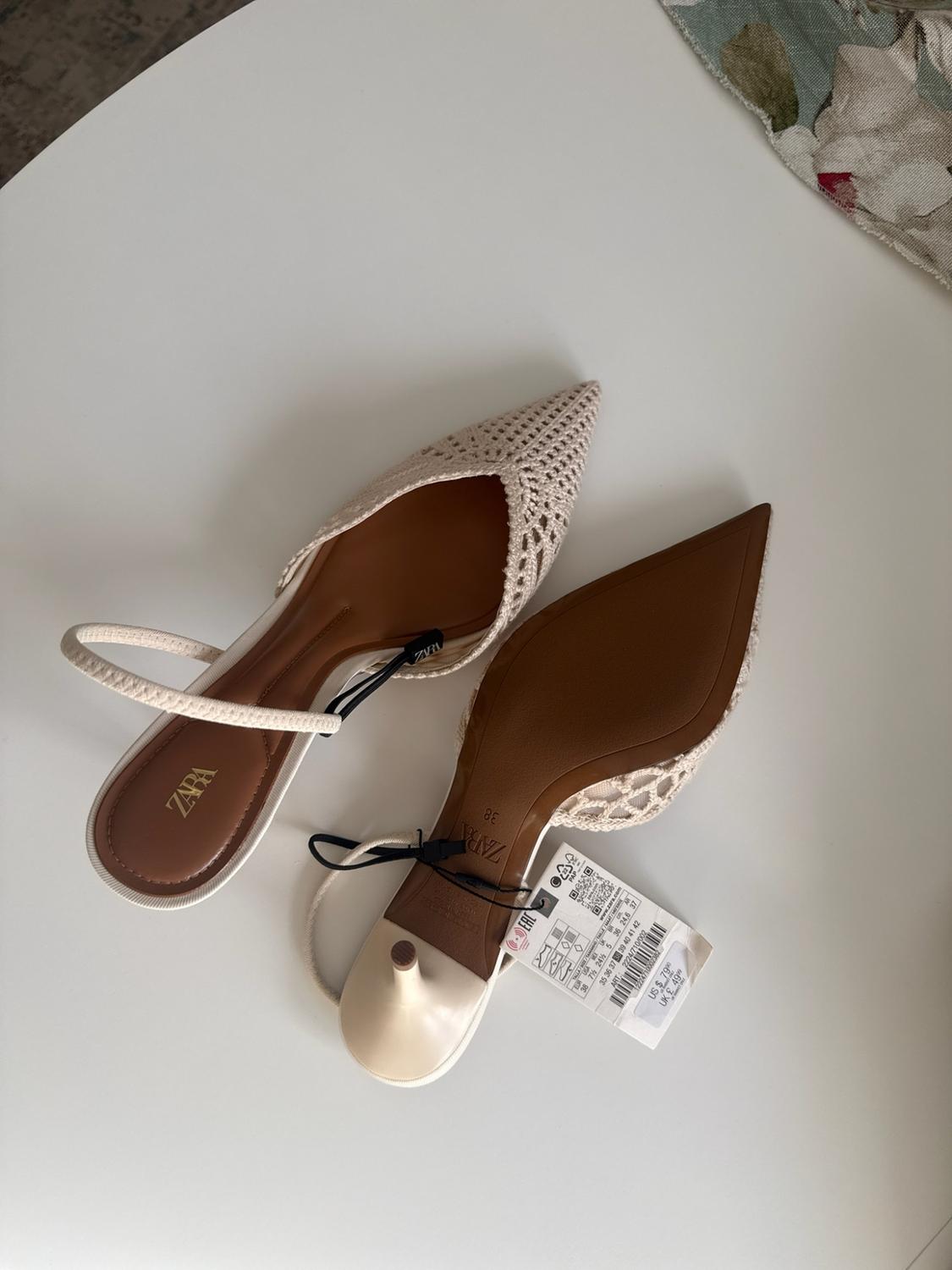 Κρεμ παπούτσια ZARA με χαμηλό τακούνι και ανοιχτό πίσω μέρος, από διάτρητο ύφασμα σε λευκό φόντο. Το ένα παπούτσι δείχνει τη σόλα και τις ετικέτες του.