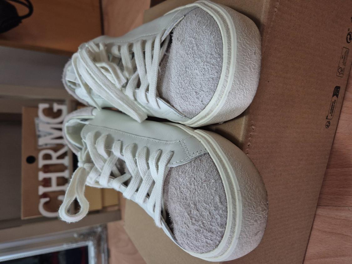 White chunky-soled trainers on a cardboard box. Background with partially visible "CHRMG" lettering.