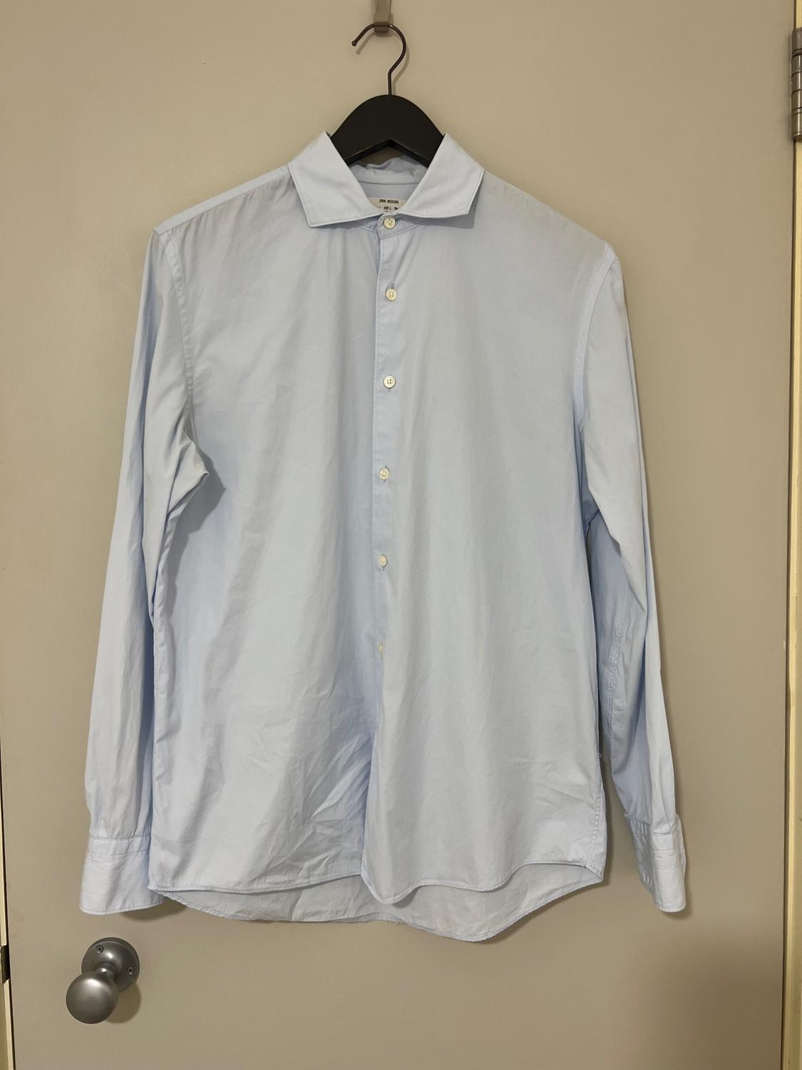 Light blue dress shirt with white buttons hanging on a black hanger over a beige door.