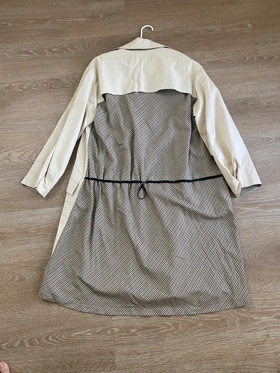 Beige coat with a black and white checkered bottom, hanging on a hanger over a light wood floor.