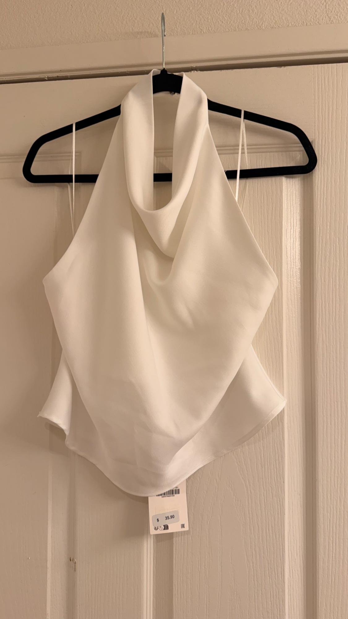 White halter-neck top with a draped neckline, hanging on a black hanger over a white door. Tag with the price $35.90.