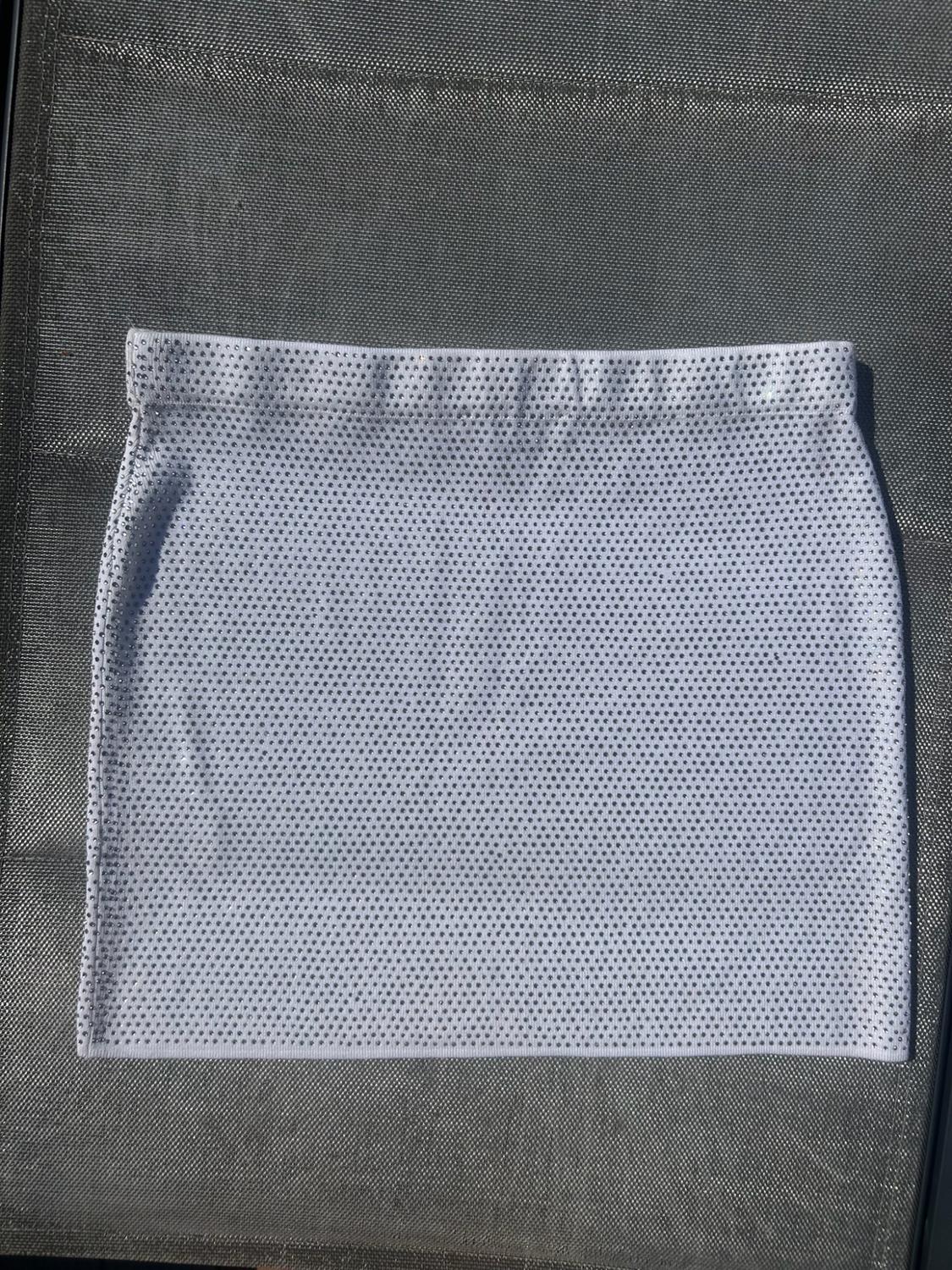 White miniskirt covered in tiny sparkles, photographed flat on a textured dark surface in natural light.