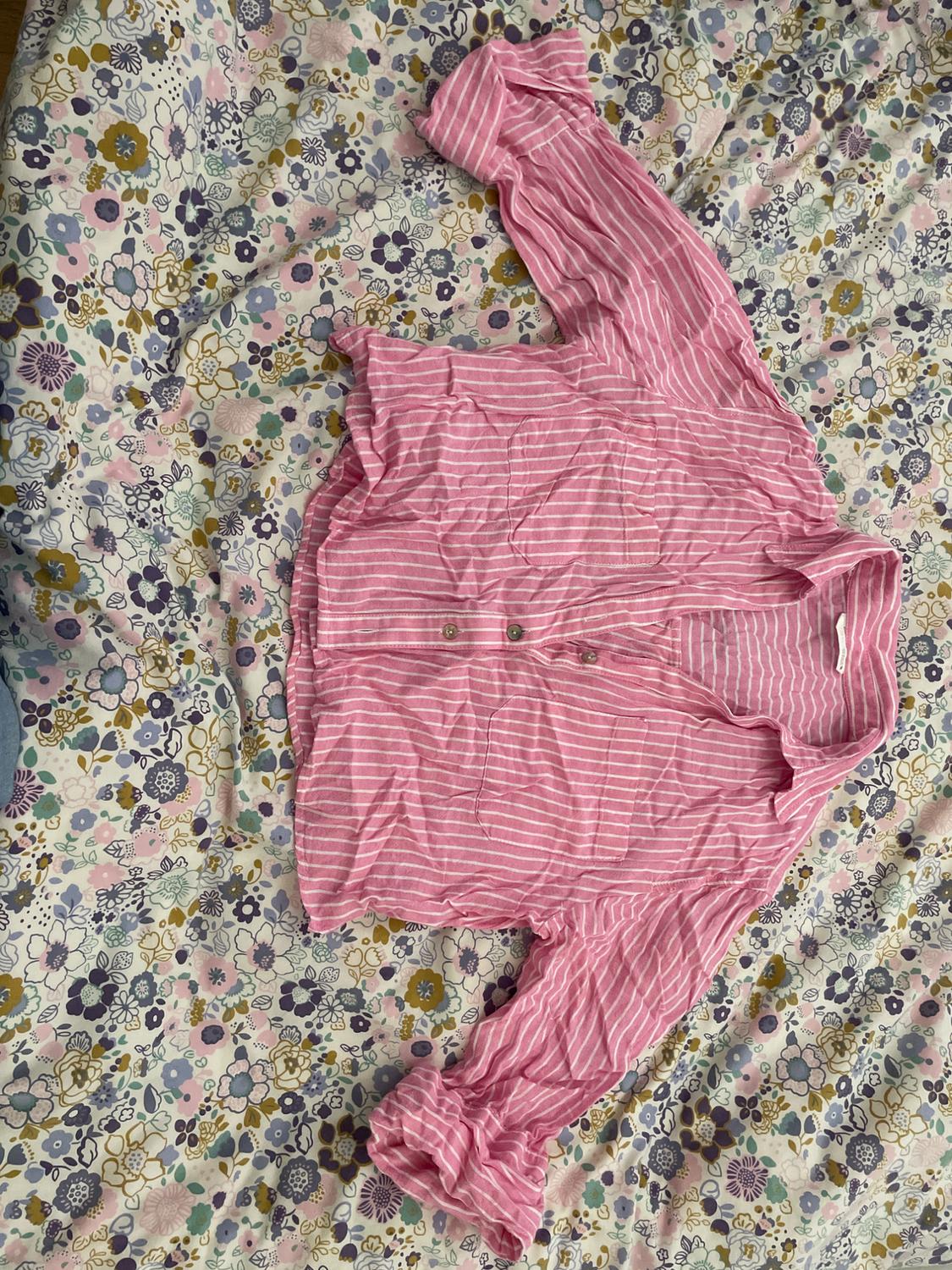 Pink shirt with white stripes and buttons, placed on a floral bedspread in pastel shades.