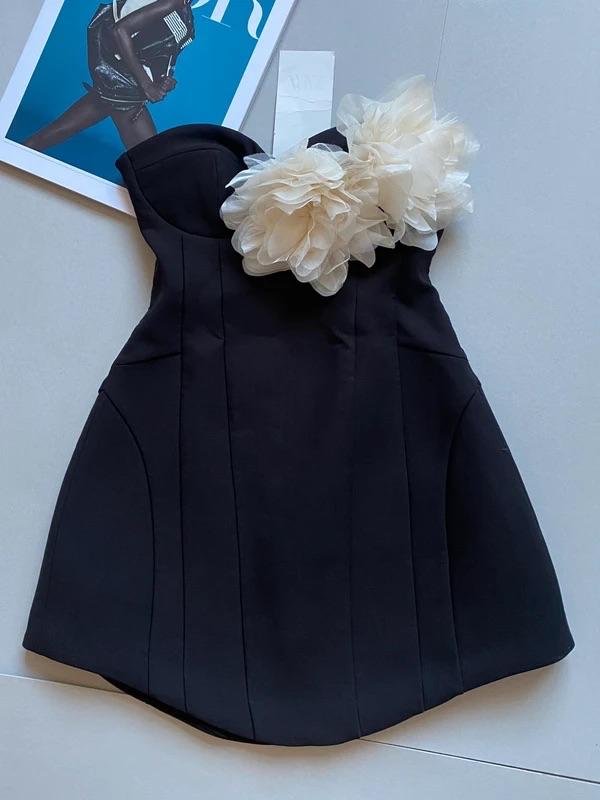 Strapless black dress with white flowers on the bust, against a grey background. Magazine with a model on the cover next to it.