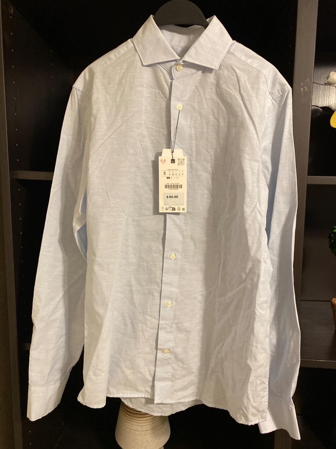 Light blue dress shirt hanging on a black clothes hanger, with a price tag of $69.90 visible in the centre. Dark background.