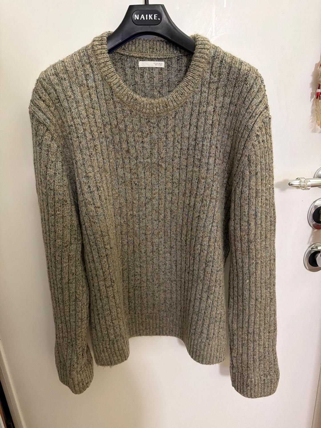 Grey knitted jumper hanging on a black hanger with the brand "NAIKE" visible. White background with a partially visible door.