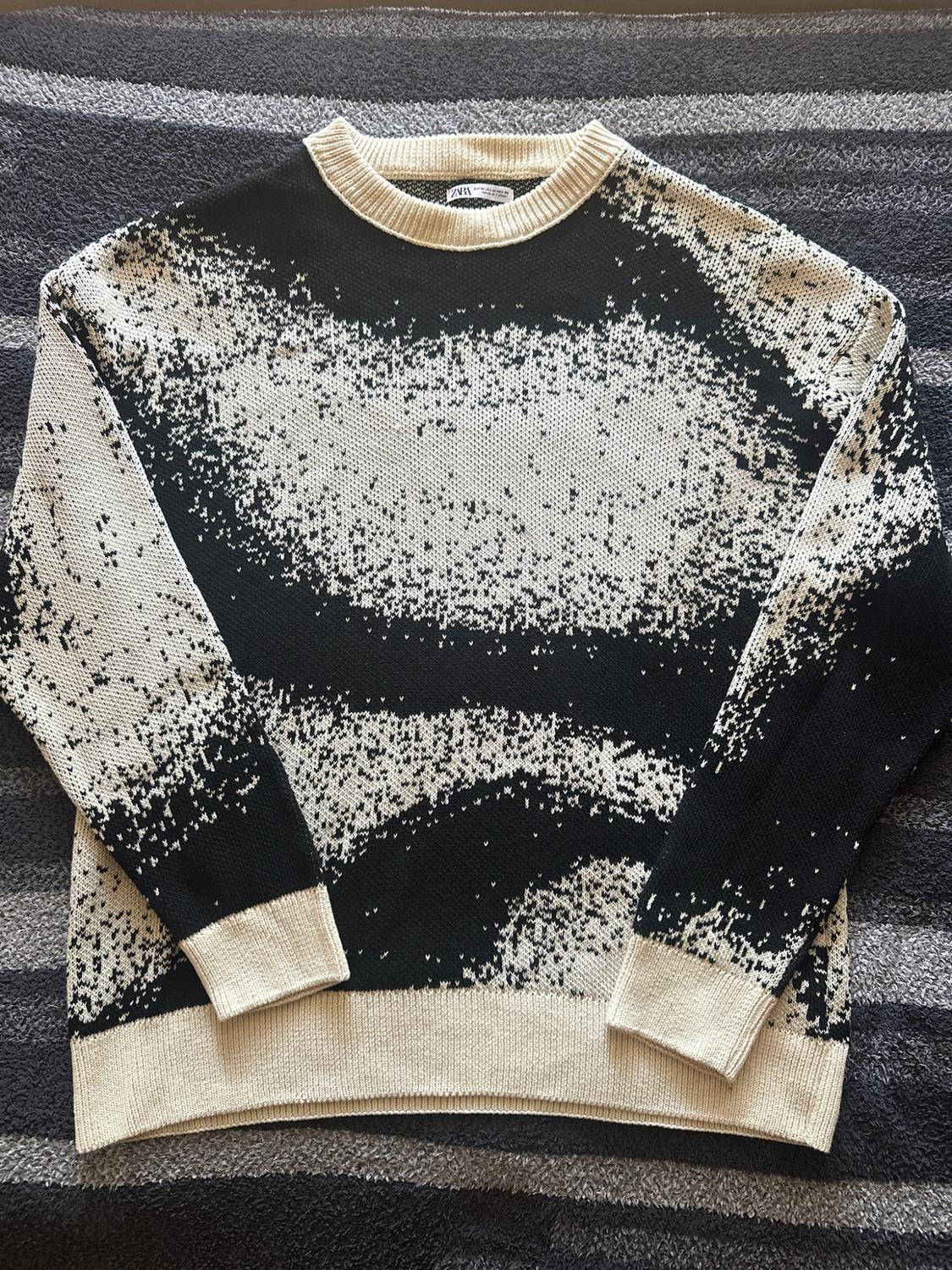 Black and cream knit jersey with a blurred abstract print, ribbed collar and cuffs. ZARA label. On a striped rug.