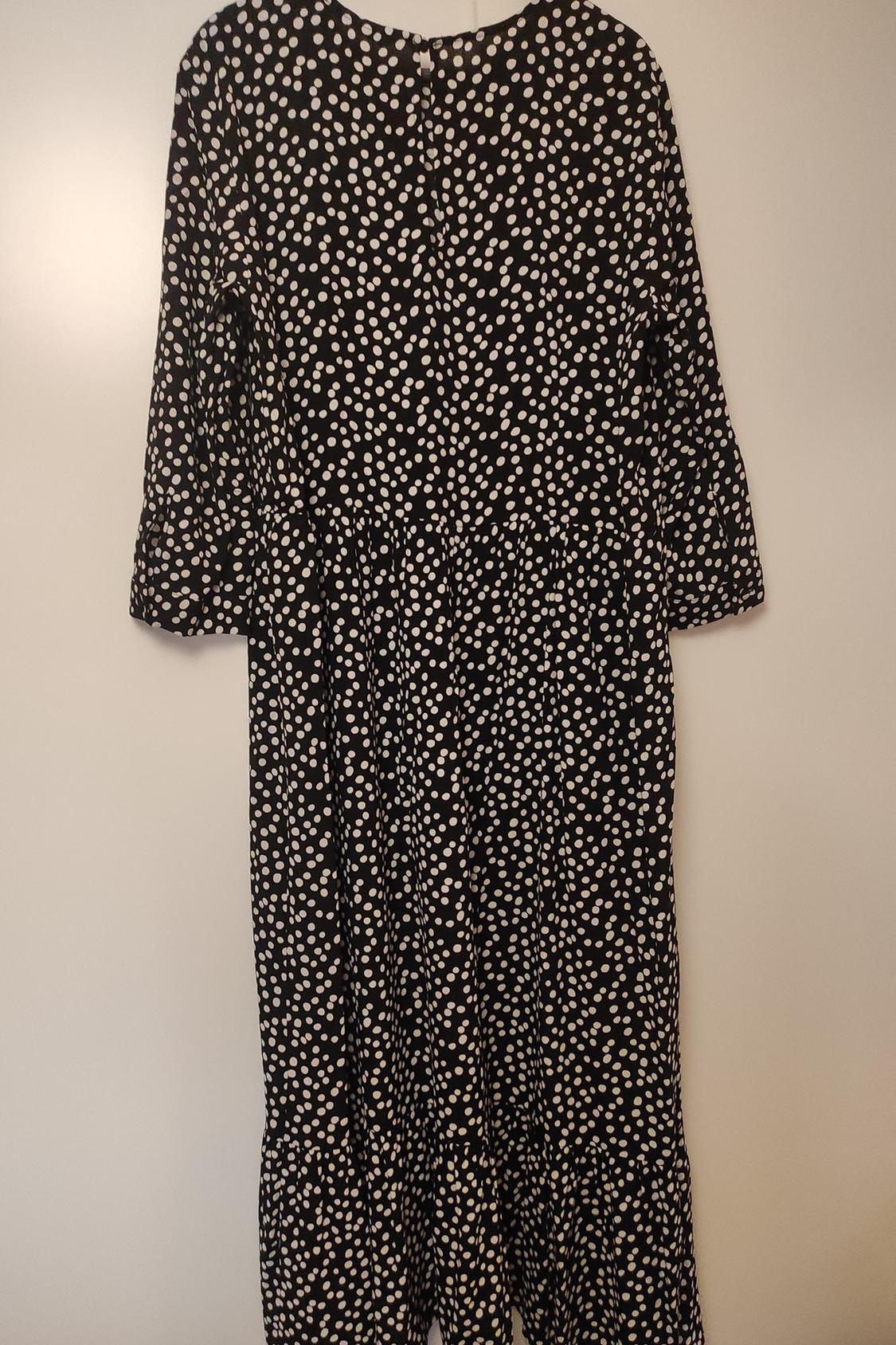 Rear view of black dress with white polka dot print, long sleeves and loose fit.