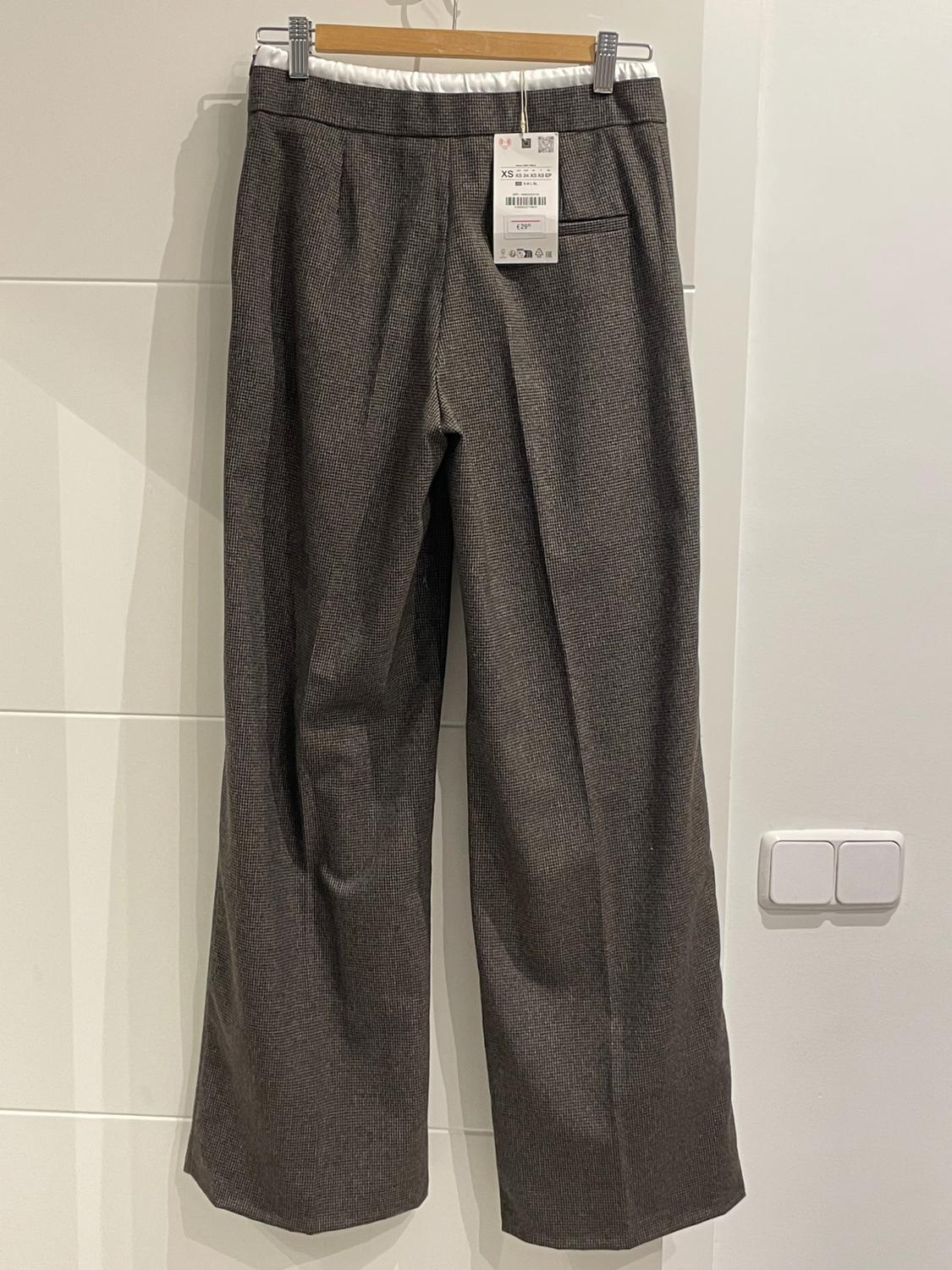 Grey fabric trousers hanging on a wooden hanger, with a visible label showing size XS and a price of €29.99. White background.