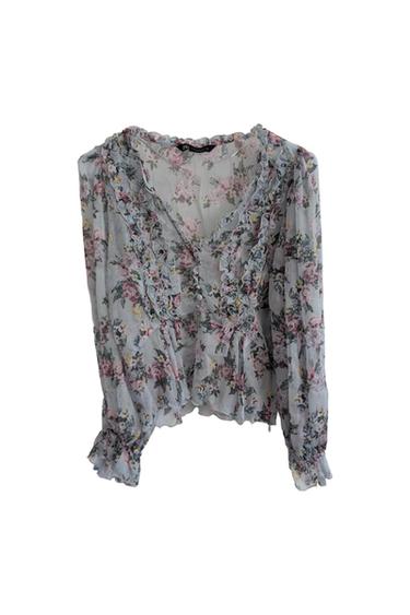 Light blue semi-sheer blouse with a floral print. V-neck with ruffles, front button closure, and long sleeves. White background.