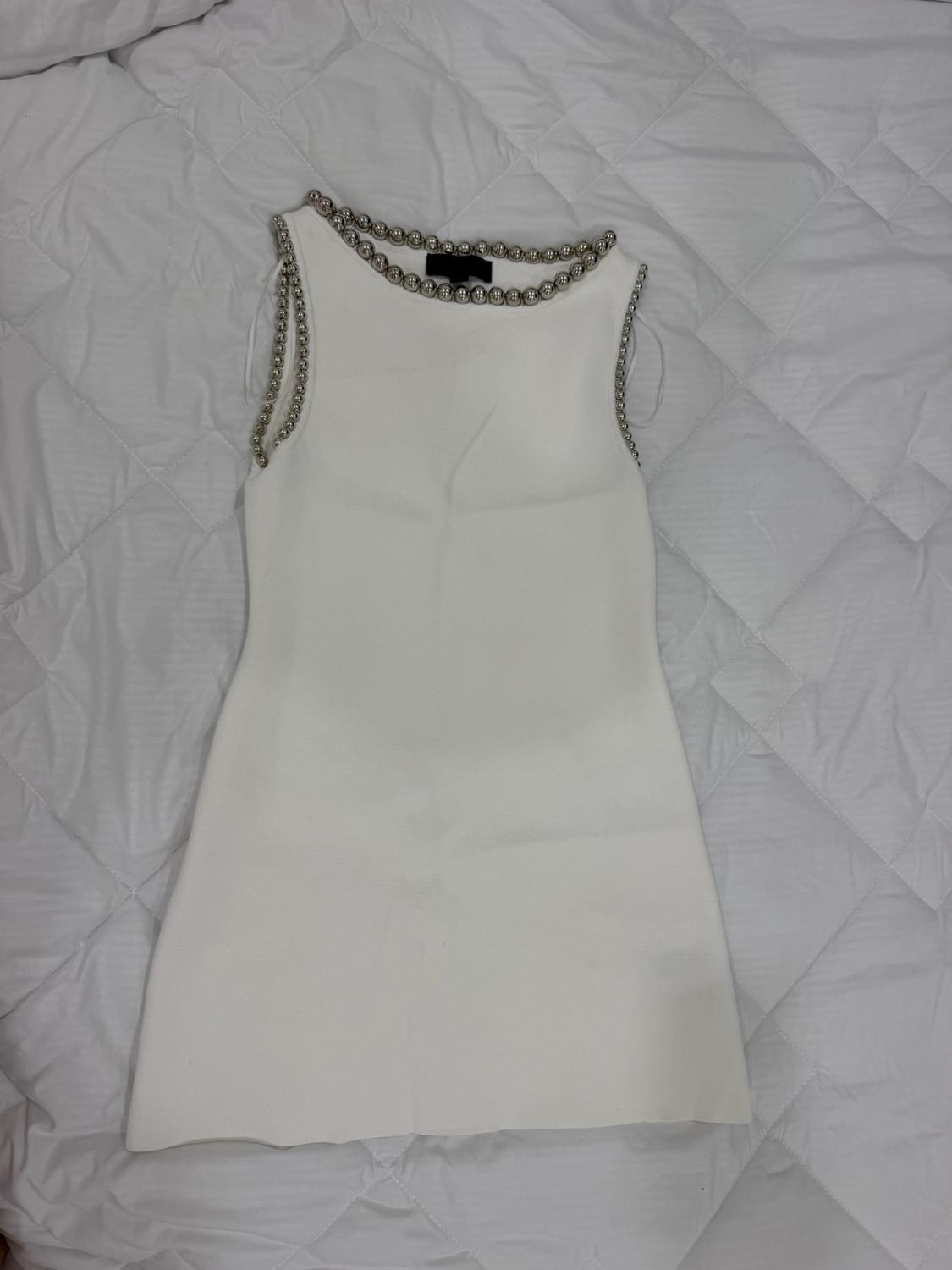 Short white sleeveless dress with silver spheres around the neckline and armholes, on a white quilted duvet.