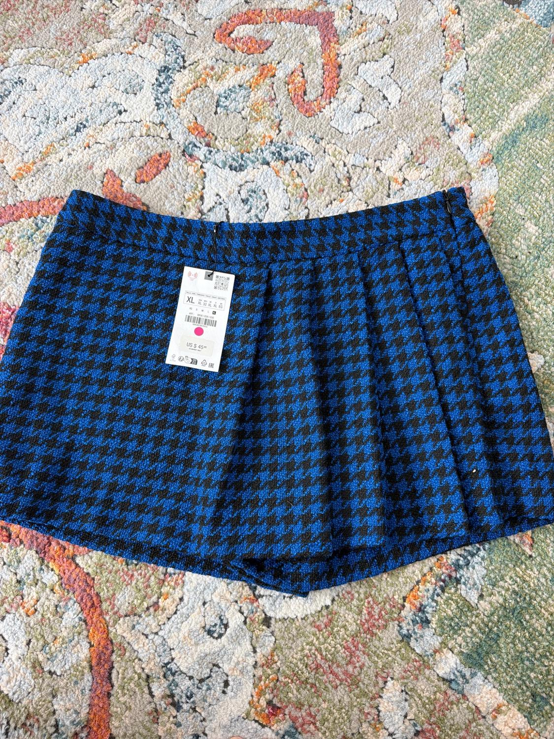 Pleated miniskirt with a blue-and-black houndstooth pattern on a carpet. Tag with the text "XL" and "US $45".