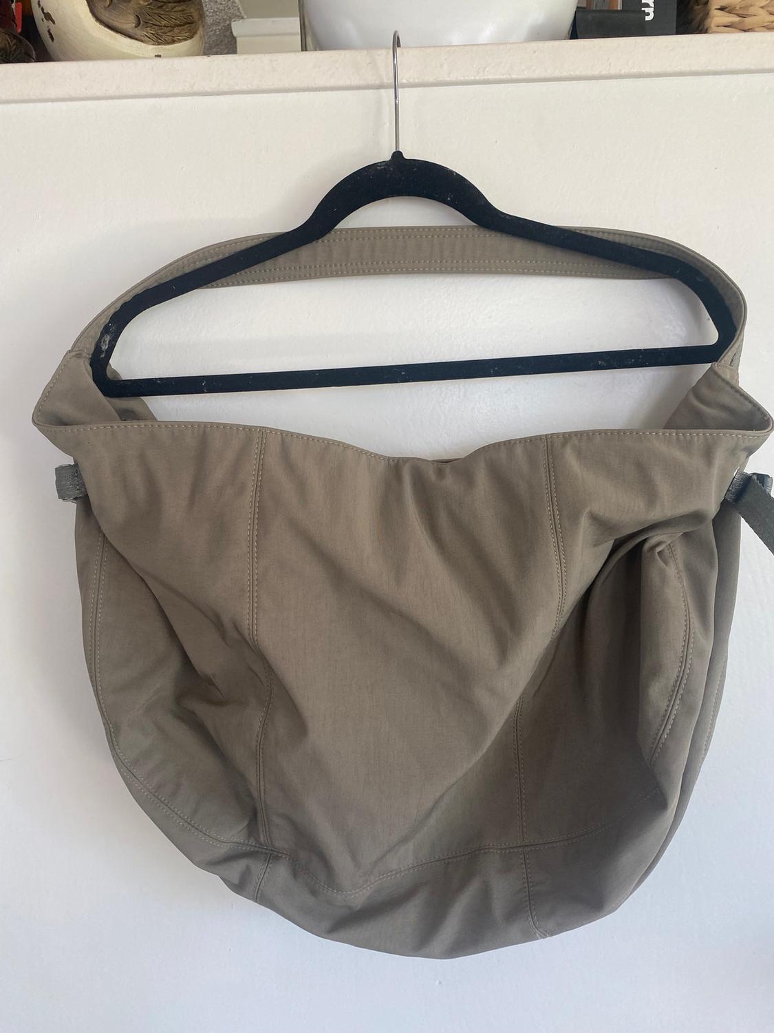 Large beige fabric bag hanging on a black hanger against a white background.
