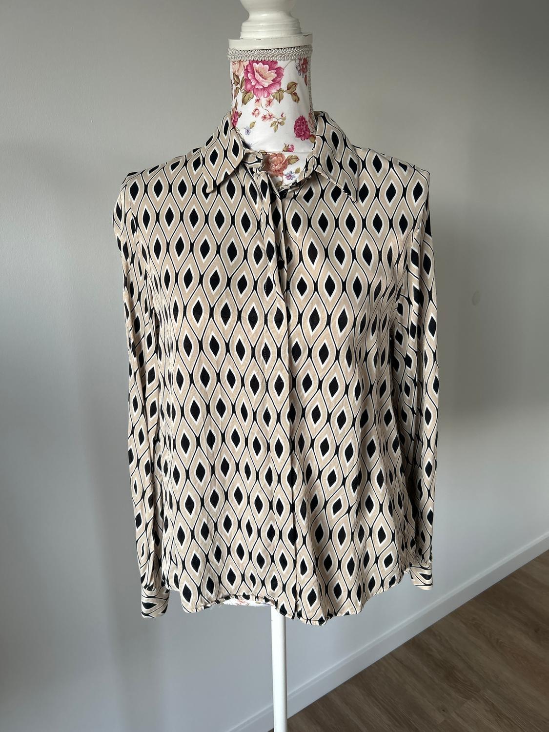 Mannequin in a long-sleeved shirt with a geometric print in beige and black tones, against a light grey background.