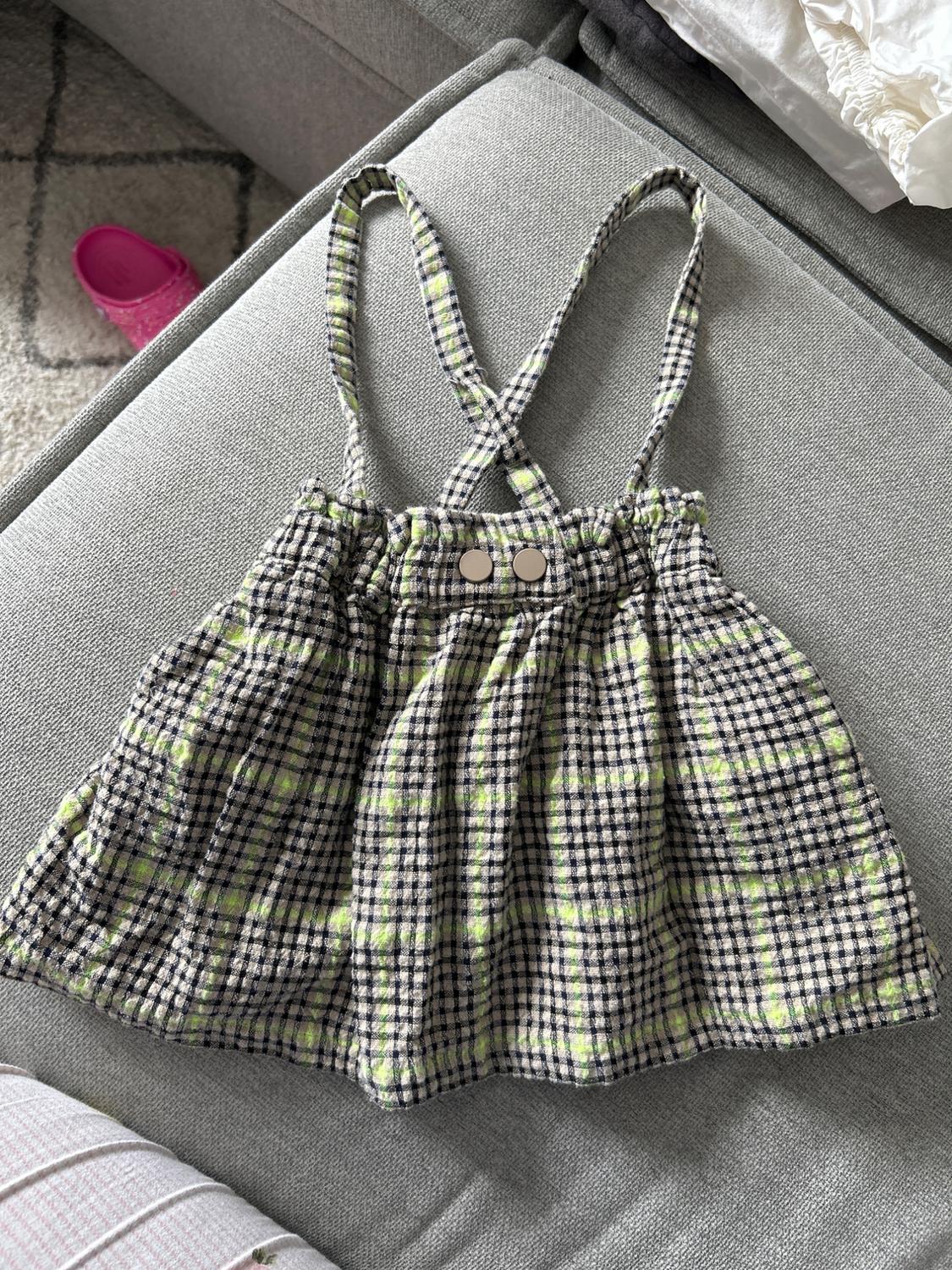 Green and black checked cross-back sundress on a grey sofa. In the background, a pink shoe.