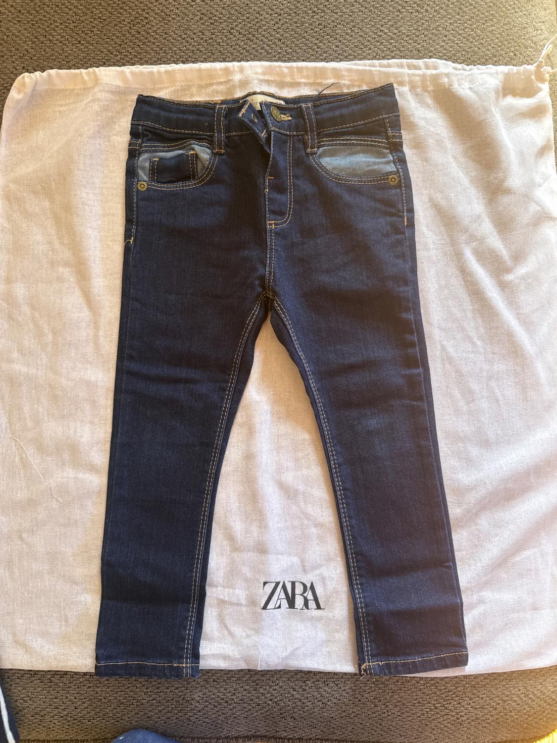 Dark denim jeans on a white fabric bag with the "ZARA" logo visible at the bottom.
