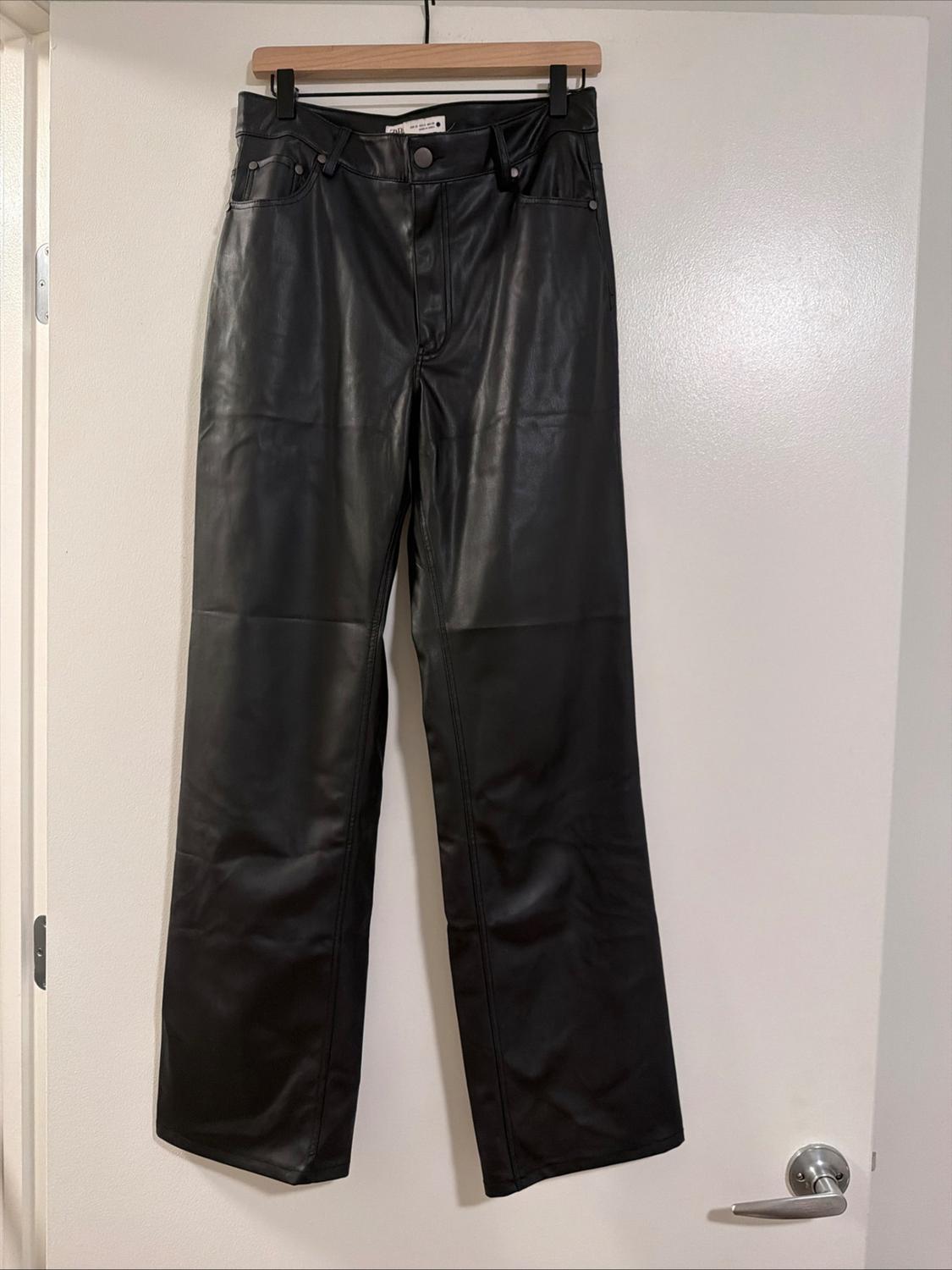 Black leather-effect trousers hanging on a wooden hanger on a white door with a silver handle.