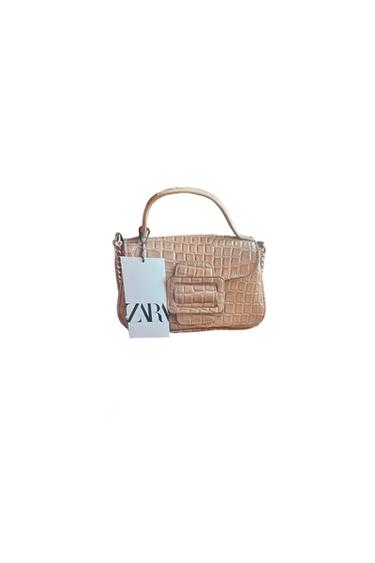 Beige handbag with crocodile texture and top handle. Hanging tag with the text "ZARA". White background.