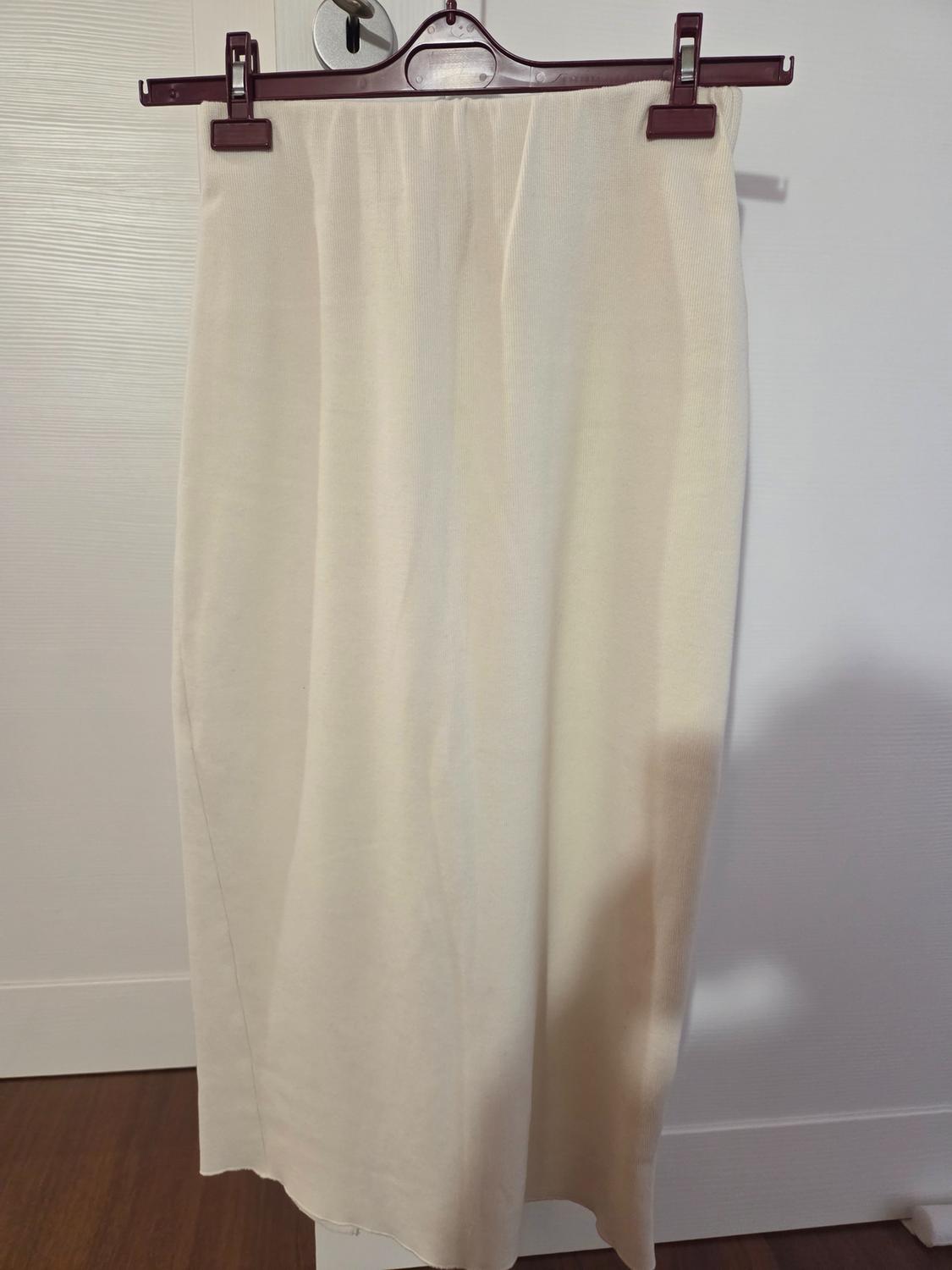 Long beige skirt hanging on a brown hanger, white background and wooden floor. The fabric is smooth and light.