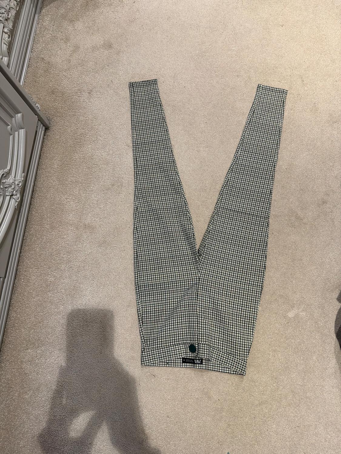 Black and white checked trousers laid out on a beige carpet, with a visible label at the bottom.