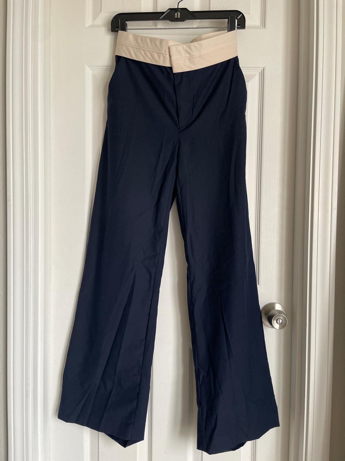 Dark blue wide-leg trousers with a beige waistband, hanging on a black hanger over a white door.
