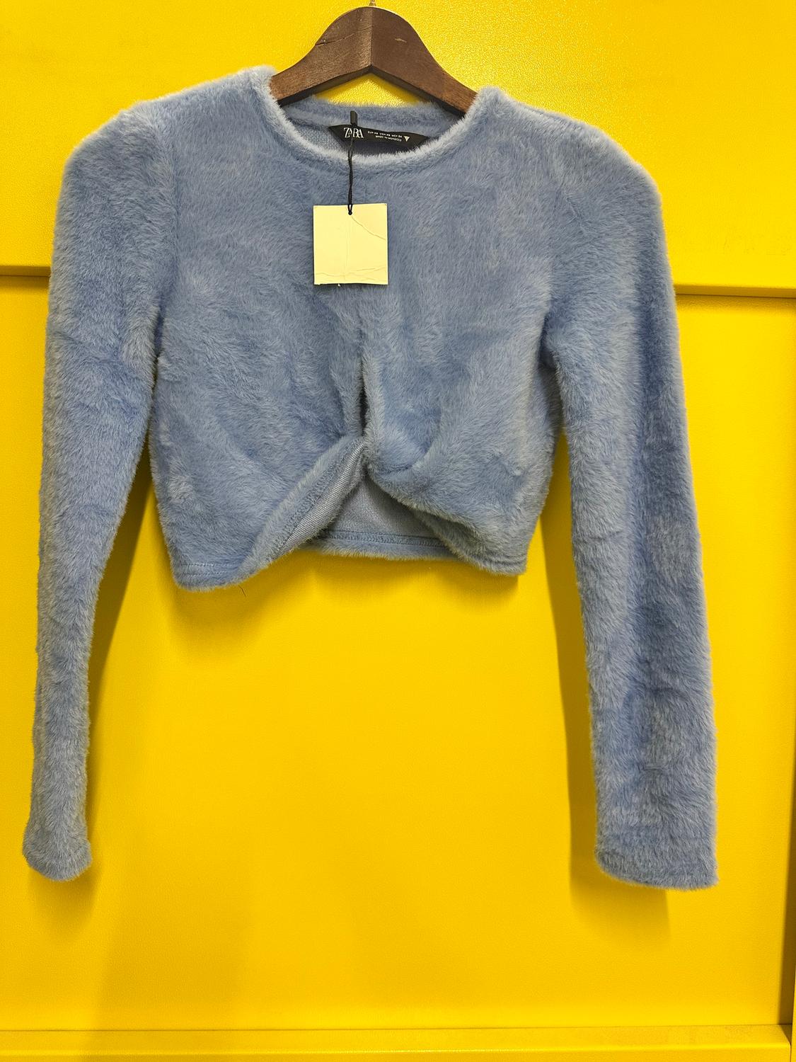 Blue marl front knot sweatshirt hanging on a wooden hanger against a bright yellow background. Label visible.