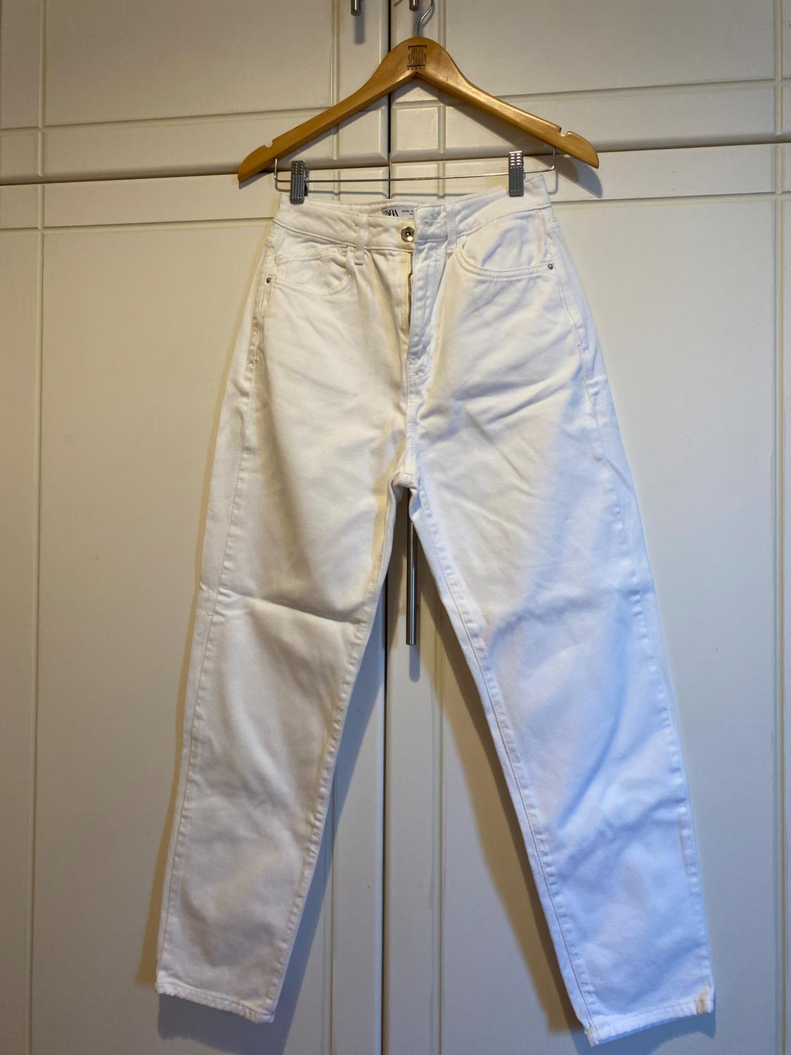 White trousers hanging on a wooden hanger in front of a white wardrobe.
