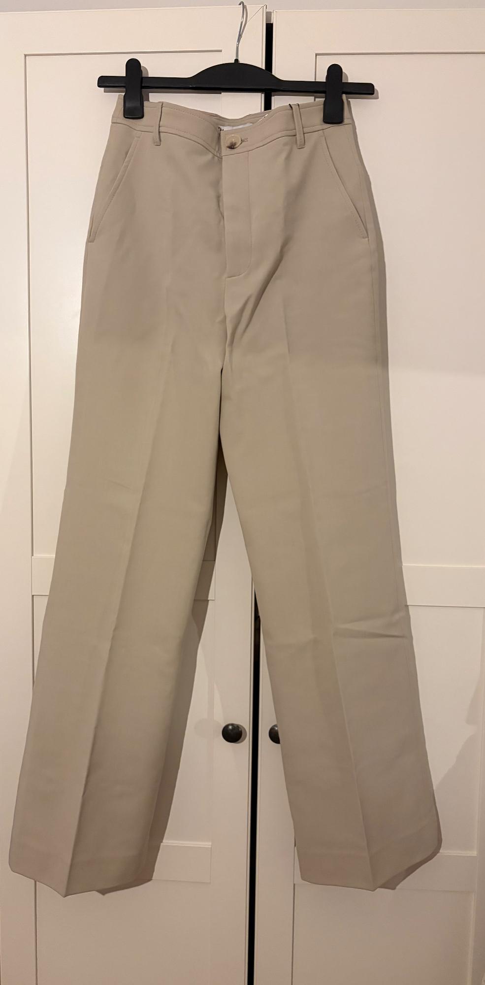 Beige straight-cut trousers hanging on a black hanger in front of a white wardrobe.