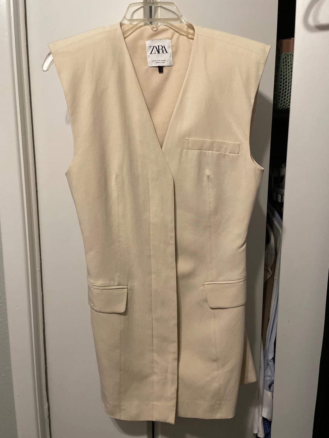 Cream sleeveless waistcoat hanging on a hanger, with a Zara label visible on the collar.