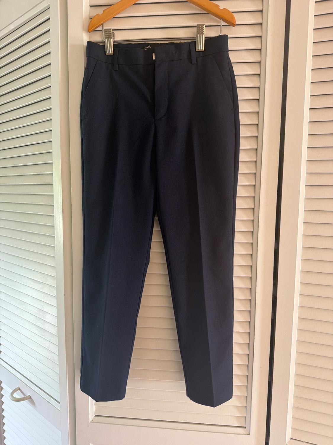 Dark blue trousers hanging on a wooden hanger against a background of white cupboard doors with blinds.