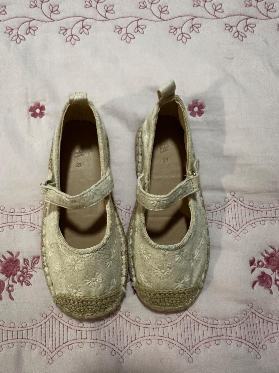 Beige embroidered fabric shoes with flowers, esparto sole, on a white bedspread with pink floral details.