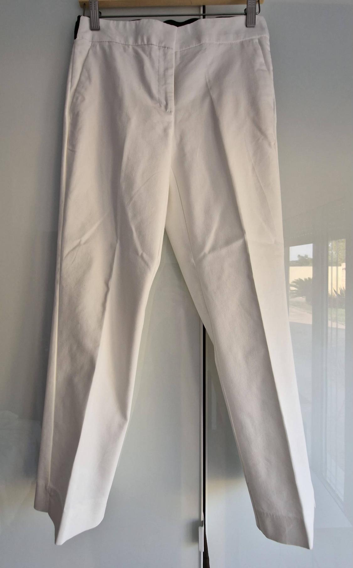 White smart trousers with a pressed crease, hanging on a hanger against a bright white background reflecting a window.