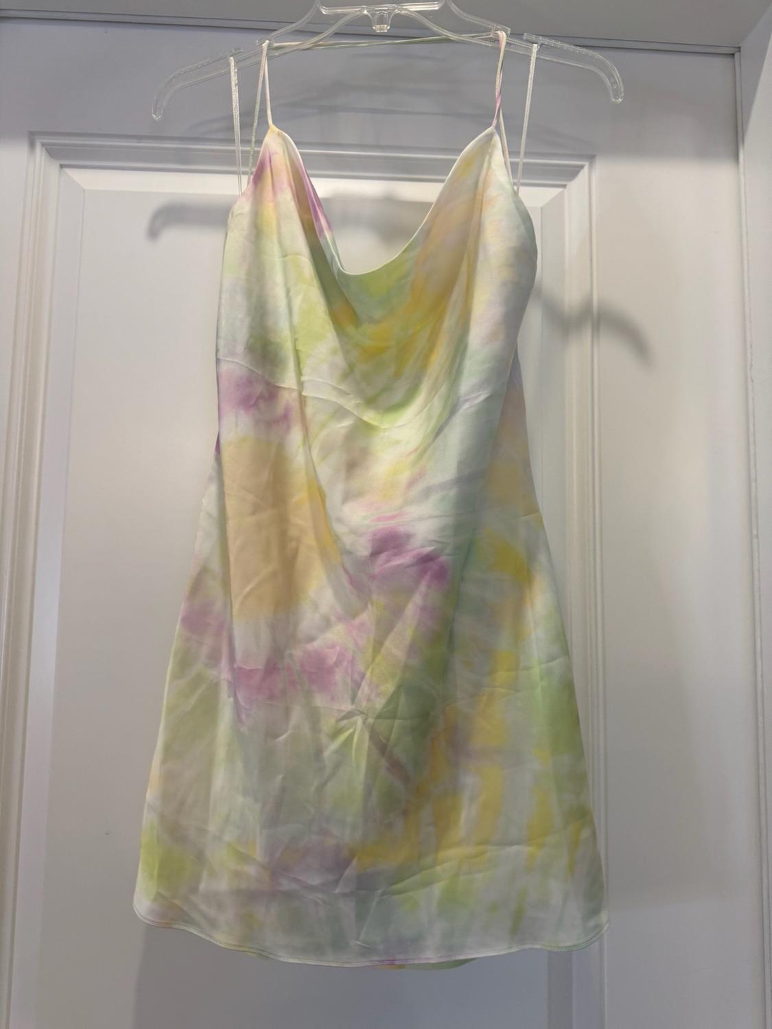 Short slip dress with a pastel print in shades of yellow, green and purple, hanging from a hanger on a white door.