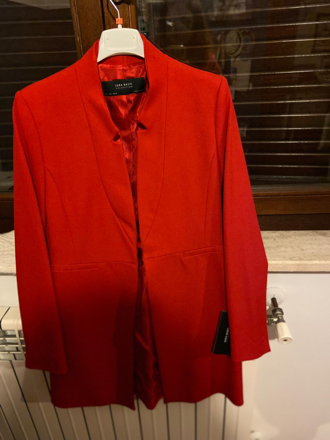 Red jacket hanging on a white hanger in front of a window. Visible label: "Zara Basic Collection".