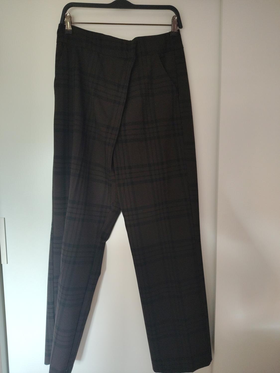 Dark checked trousers hanging on a black hanger against a white background.