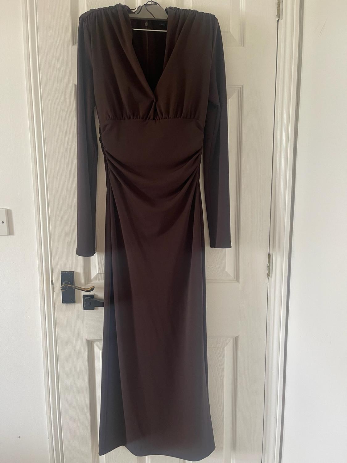 Long dark brown long-sleeved dress with a V-neckline and ruched detail at the waist, hanging on a white door.