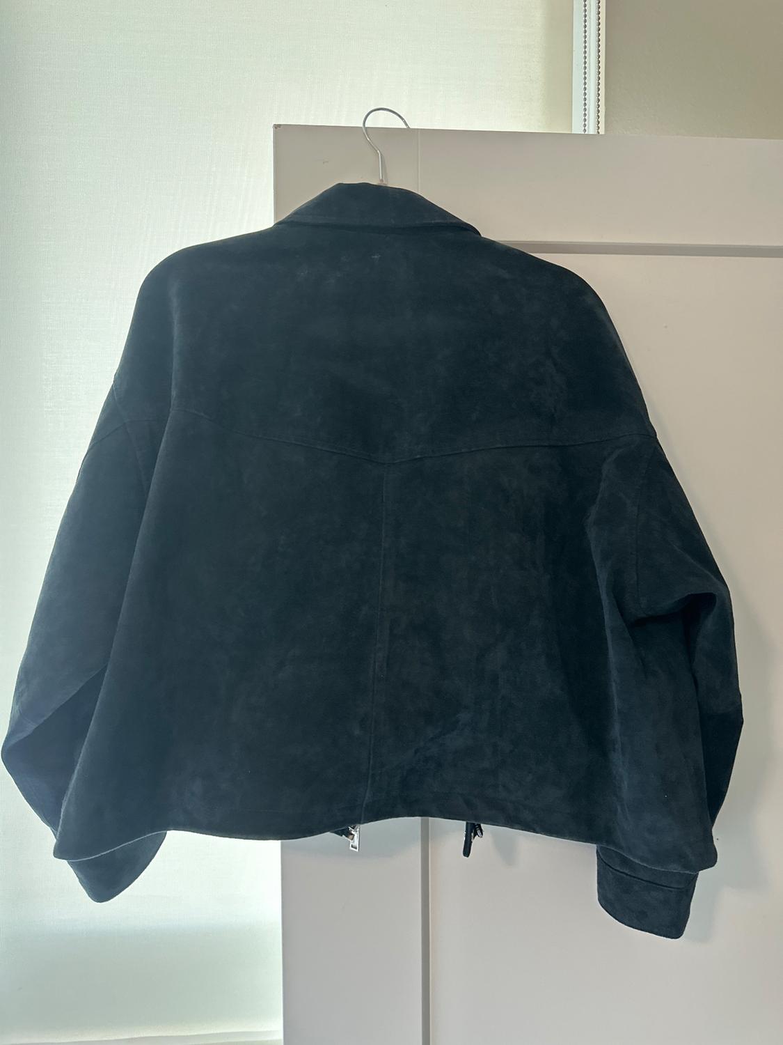Black suede jacket hanging on a white door, illuminated by natural light from a nearby window.