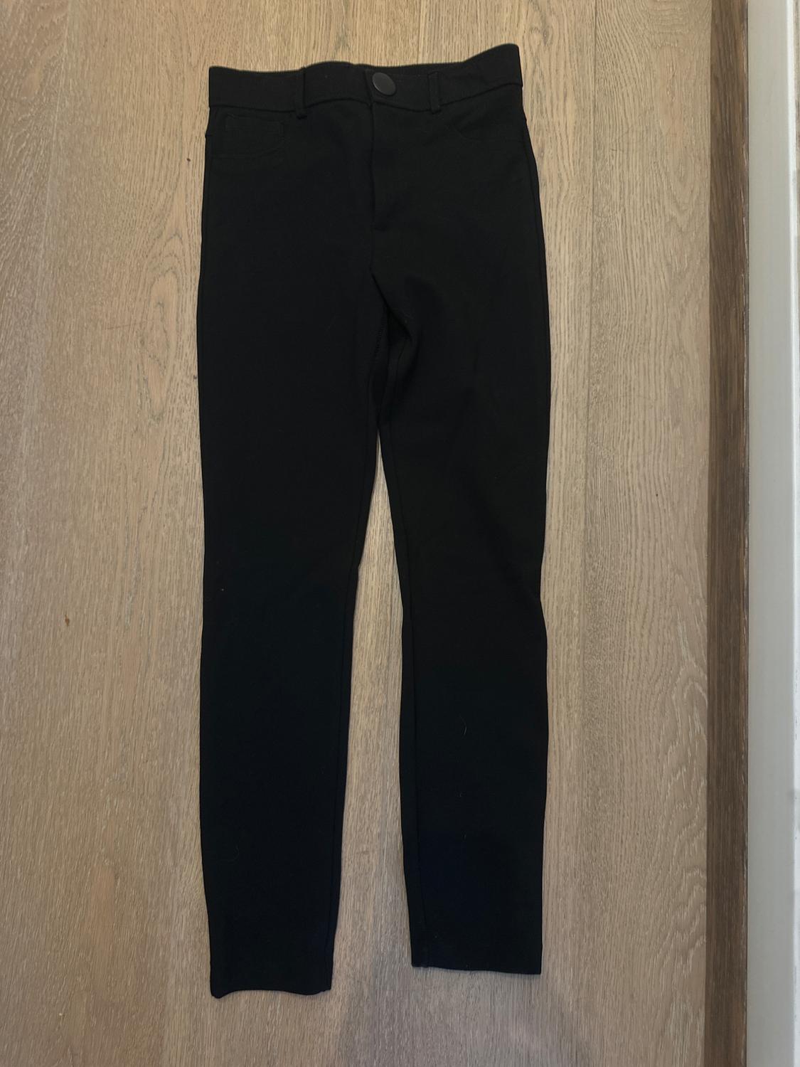 Black skinny trousers on a light wooden floor, seen from above.