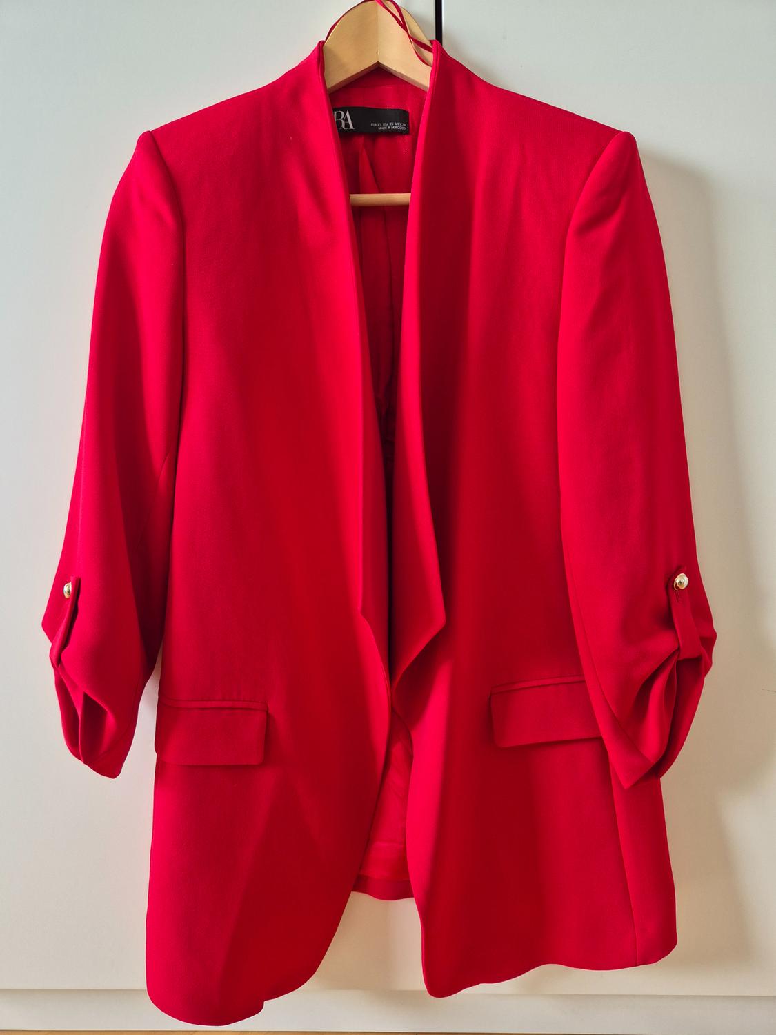 Red jacket hanging on a wooden hanger, with rolled-up sleeves and front pockets, against a white background.