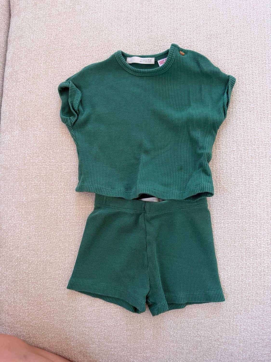 Textured green kids' outfit set with a shirt with a button on the shoulder and a pair of shorts, on a light background. ZARA text label.