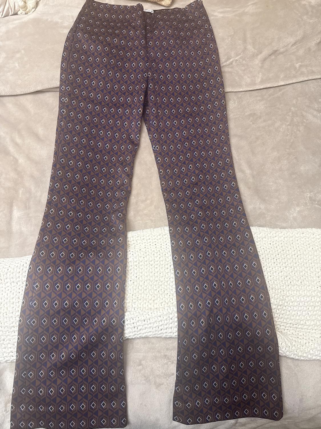 Bell-bottom pants with a geometric print in brown and blue tones, on a beige and white woven fabric surface.