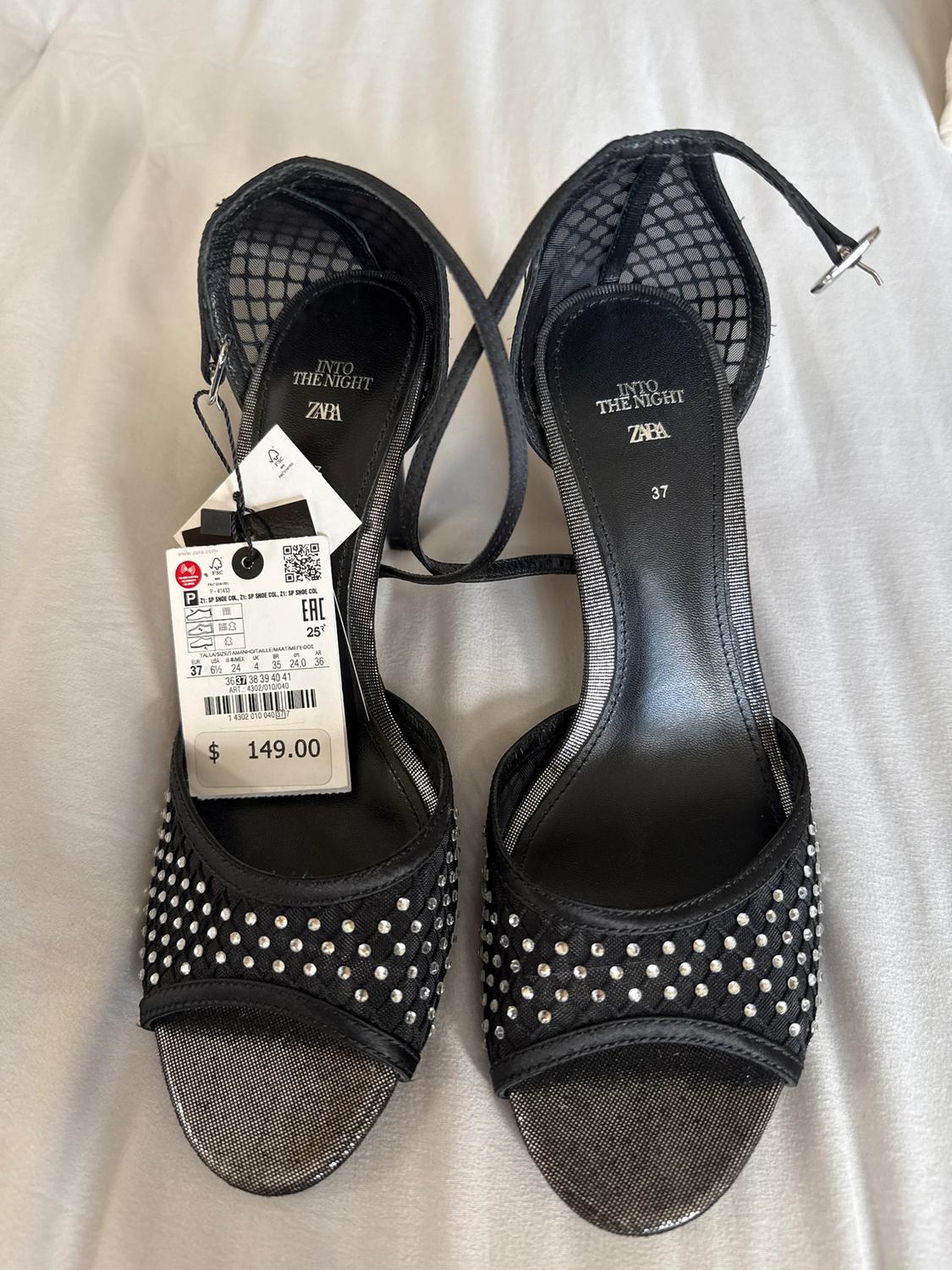 Black heeled sandals, adorned with silver studs. Price tag: $149.00. Visible text: "INTO THE NIGHT ZARA". Size 37.